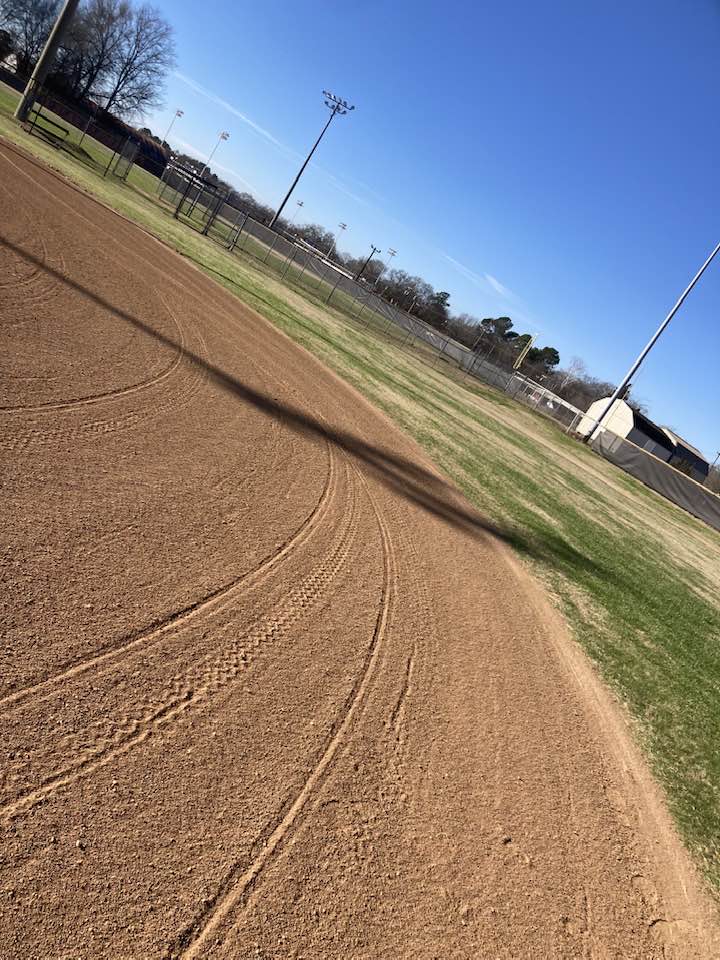 Professionally groomed baseball infield with curved rake lines under a clear blue sky